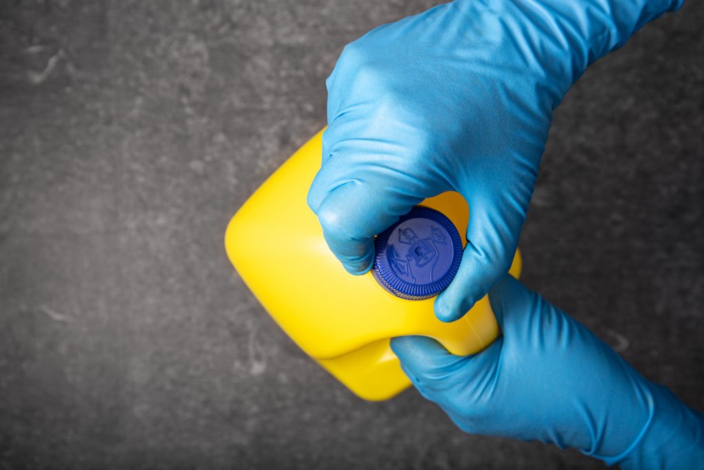 Human hand in protective glove opening a yellow bleach bottle. Disinfection concept