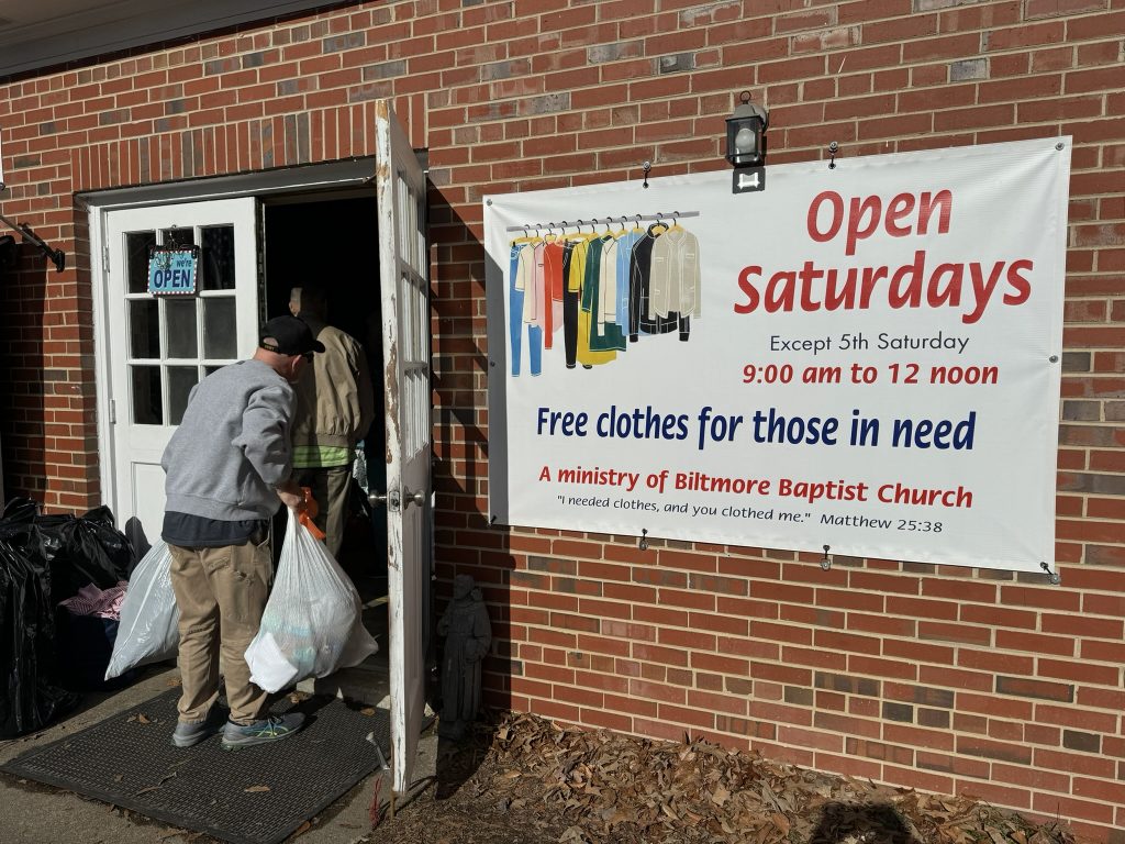 A person walks through the door of a brick building with bags of donations